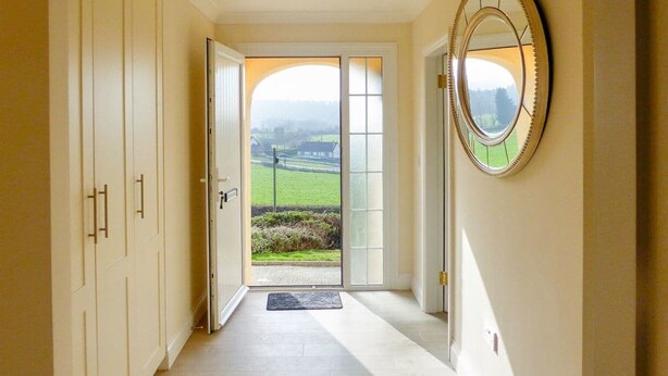 A hallway with a view of a green landscape through a glass door, a mirror on the wall, and a ceiling light fixture. - Bolams Holiday Home (Thomastown)