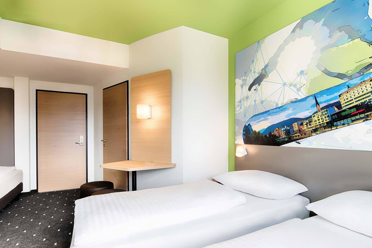 A hotel room with a bed, a desk, and a wall-mounted TV.