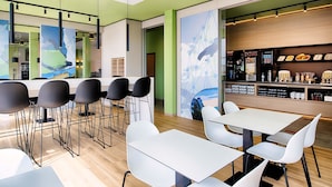 Un café moderno con zona de bar, diferentes disposiciones de asientos y un mural en la pared.
