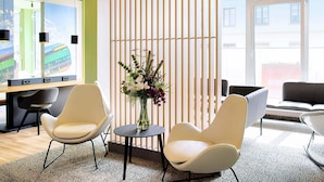 Un espacio de oficina moderno con dos sillas blancas, una pequeña mesa redonda con un florero y una partición de listones de madera.