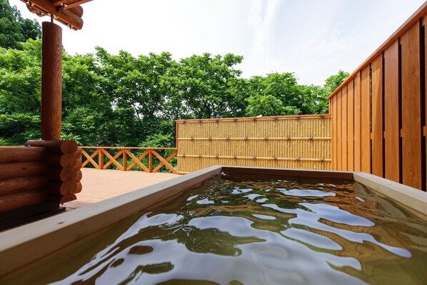 Une terrasse en bois avec un bain à remous alimenté par une source d’eau chaude, entourée d’une clôture en bambou et de murs en bois.