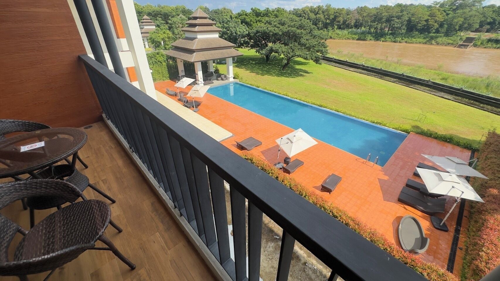 Un balcon avec piscine, un espace salon extérieur et une vue sur un jardin et une rivière.