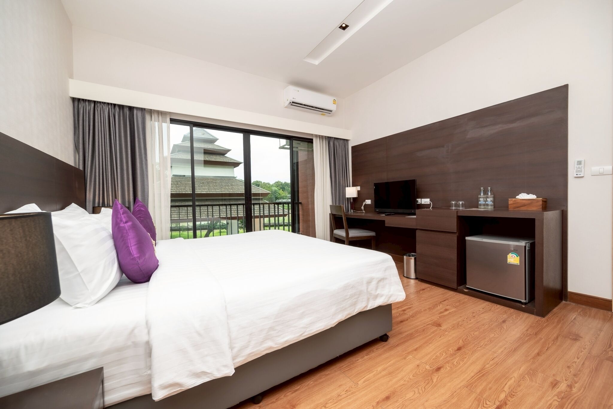A hotel room with a bed, a desk, a TV, and a minibar.