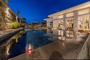 A luxurious pool area with a stone wall, lounge chairs, and a well-lit deck.