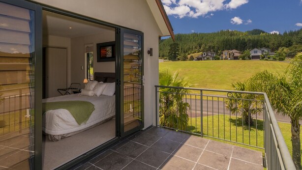 A bedroom with a bed, a nightstand, and a window. - Villa 51 - Pauanui Holiday Home (Pauanui)