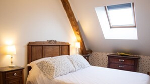 A bedroom with a wooden headboard, a bed with white bedding, a nightstand with a lamp, a dresser, and a window with a view.