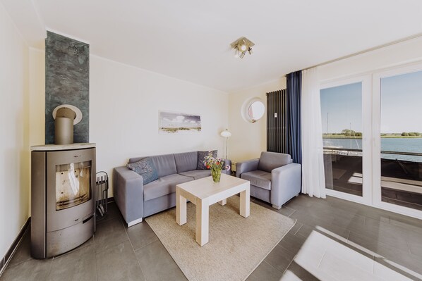 Ett modernt vardagsrum med en soffa, ett soffbord, en öppen spis och utsikt över havet genom stora fönster.