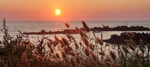 Un coucher de soleil sur une côte rocheuse, avec de l’herbe au premier plan.