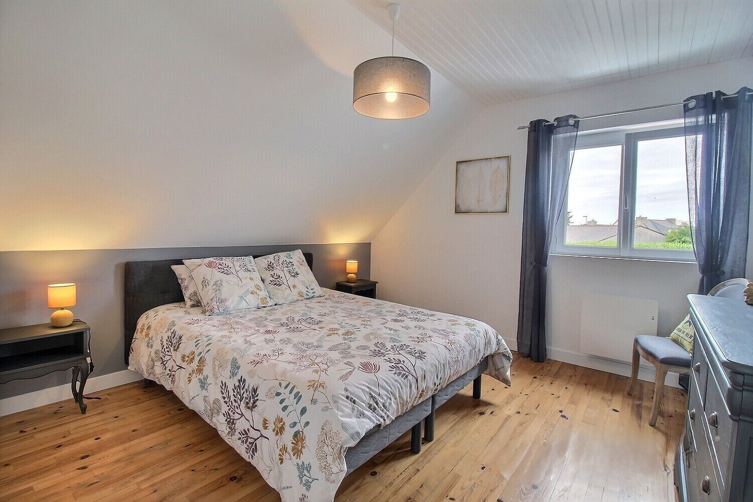 A bedroom with a bed, bedside lamps, a window with curtains, and a view of the outside.