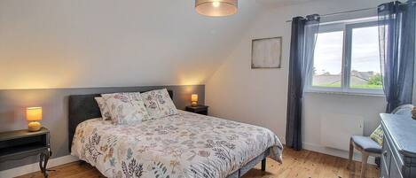 A bedroom with a bed, bedside lamps, a window with curtains, and a view of the outside.