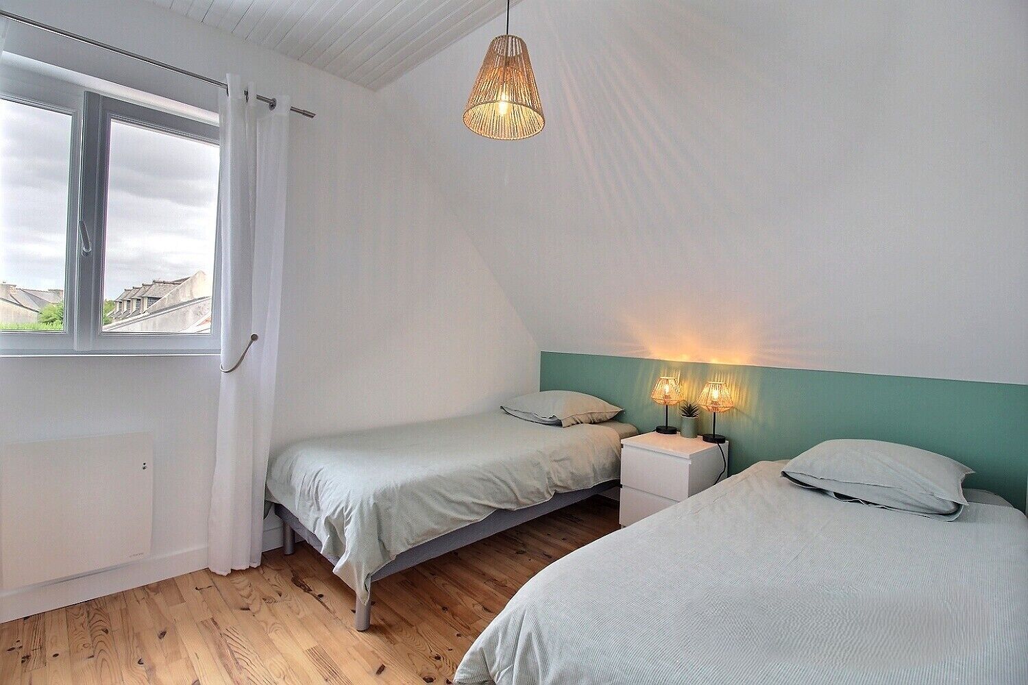 Une chambre avec deux lits, une fenêtre et un luminaire suspendu.