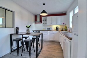 Eine Küche mit weißen Schränken, einer Holz Arbeitsplatte, einer schwarzen Pendelleuchte und einem Essbereich mit Sitzhocker.