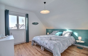 A bedroom with a bed, a bedside table, a window with curtains, a radiator, and a hanging light fixture.