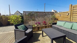 Une terrasse extérieure avec des meubles en osier, une clôture en bois et des parterres de fleurs.