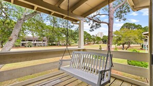 A wooden swing bench under a covered porch with a view of a park and buildings. - Seascape Resort Villa - Our Happy Place (Miramar Beach)