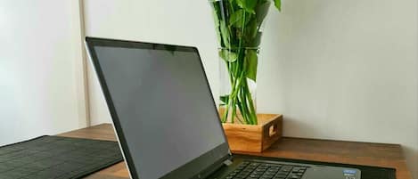 A laptop on a desk with a magazine and a vase of flowers in the background.