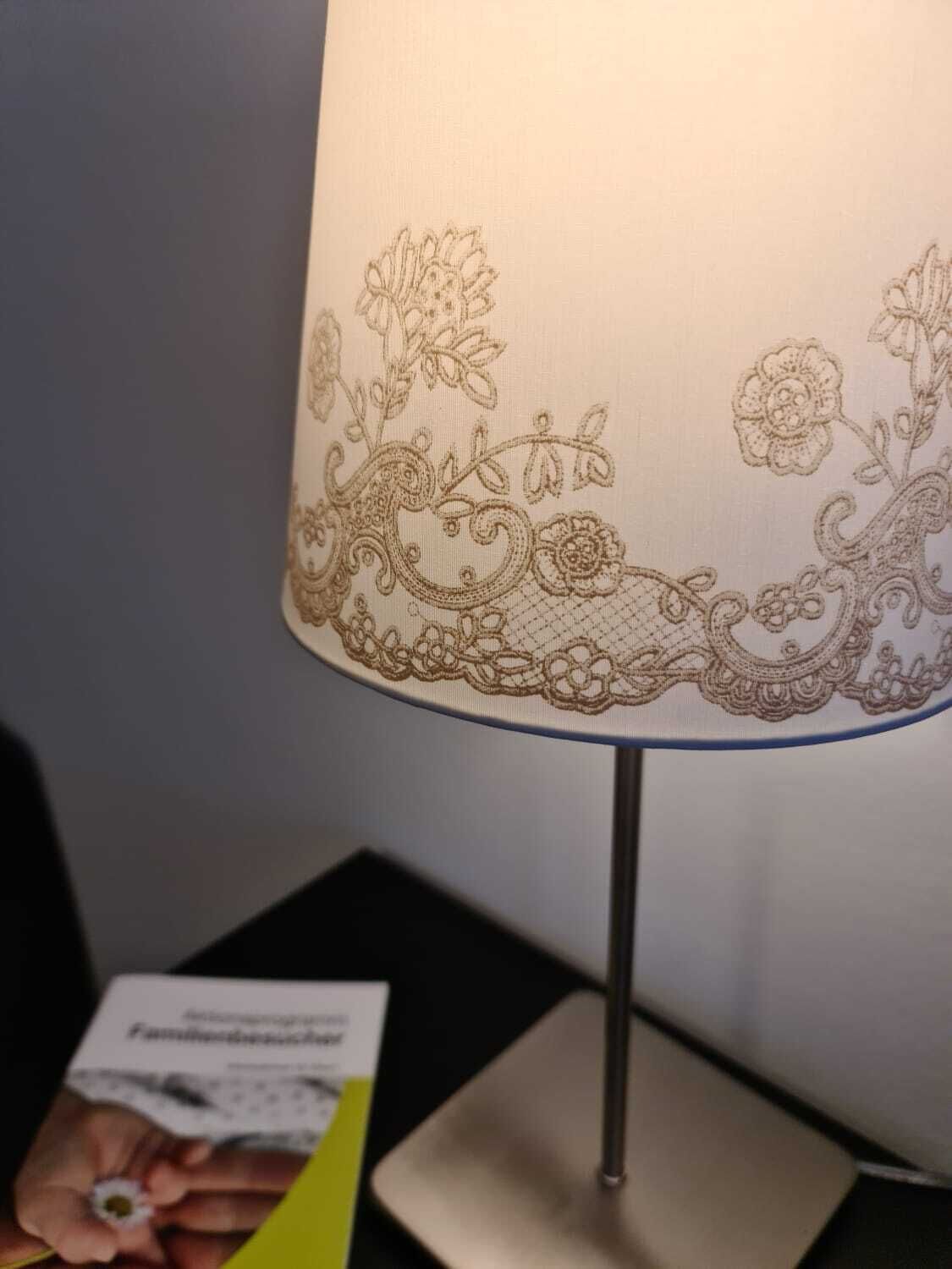 En bordlampe med en dekorativ stofskærm med blomster- og paisley-mønstre.