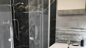 Un baño moderno con ducha envuelta en vidrio, un lavabo blanco y un protector contra salpicaduras de mármol.