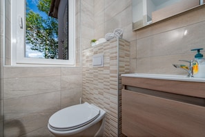 A modern bathroom with a toilet, a sink, and a window with a view of trees. - Villa Meštrovic (Zadar)