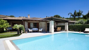 A poolside area with a clear blue pool, outdoor seating, and a building with a tiled roof.