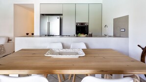 A modern kitchen with a central island, white cabinetry, and a dining area with a wooden table and white chairs.