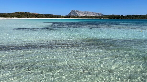 A clear coastal view with a mountain in the background.