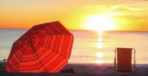 Escena de platja amb un parasol a ratlles i una cadira de platja.