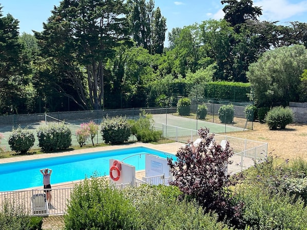 Ein Pool, umgeben von Grünflächen, und ein Tennisplatz.