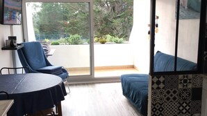 Une pièce comprenant une table à manger, des chaises, un canapé et donnant sur un espace verdoyant grâce à une porte-fenêtre coulissante.