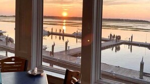 Vue depuis l’intérieur d’un bâtiment doté de grandes fenêtres donnant sur une marina au coucher du soleil.