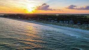 Un paysage côtier avec une plage, l’océan et une zone résidentielle, au moment du coucher du soleil.