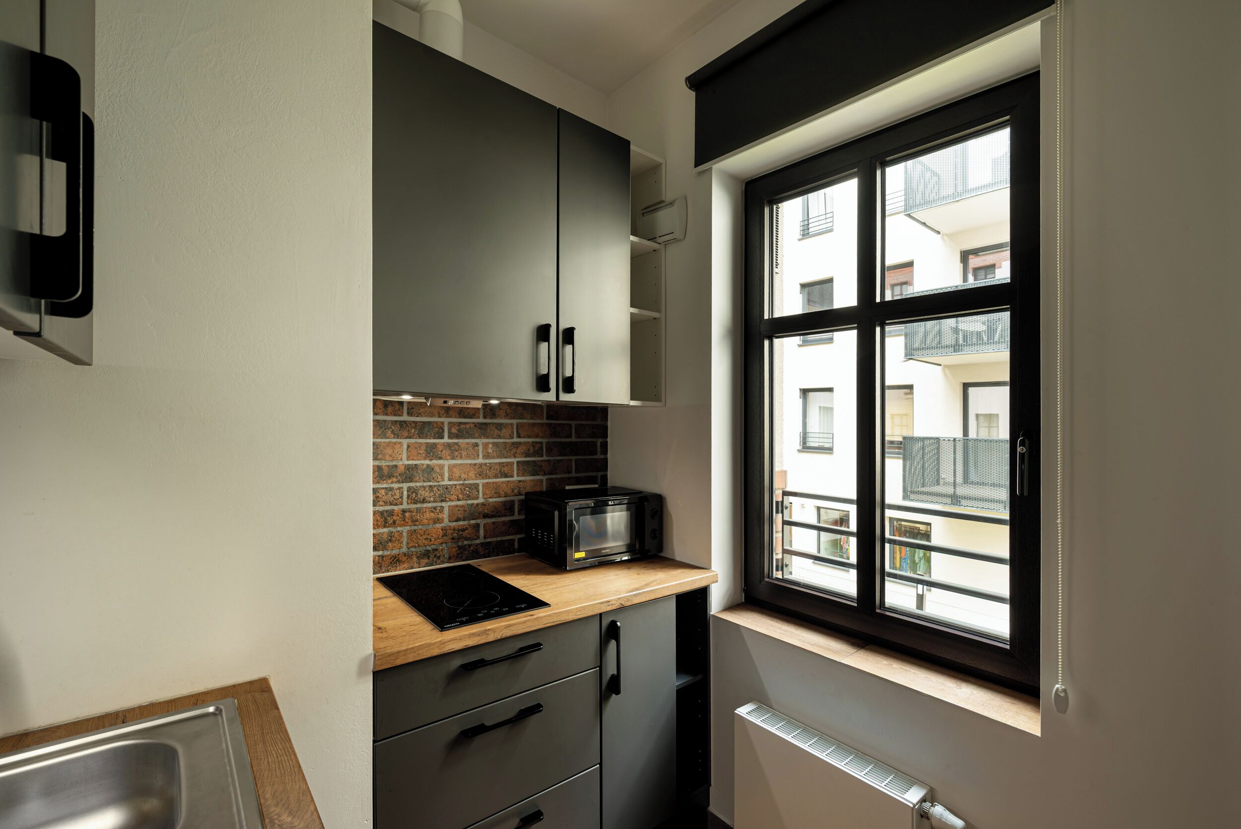 Una cocina compacta con microondas, un lavamanos y una ventana con vistas a edificios.