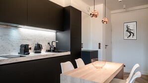 Une cuisine moderne avec des meubles de couleur sombre, un plan de travail en marbre et une table à manger en bois, accompagnée de chaises blanches.