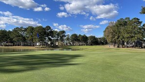 Un campo de golf con un estanque, árboles y casas al fondo.