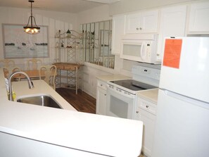 A compact kitchen with white cabinetry, a stainless steel sink, a microwave, a stove, and a refrigerator. - Family Friendly Villa 1202 with 27 Hole Golf Course Available and Great Resort Amenities by RedAwning (Calabash)