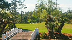 Un puente de madera que conduce a un campo de golf con una cerca blanca a un lado.
