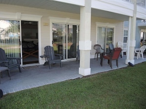 A covered outdoor seating area with chairs and tables, a sliding glass door entrance, and a grassy lawn. - 1202m 1 Bedroom Condo by RedAwning (Calabash)