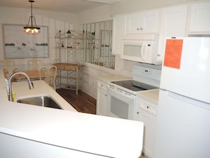 A compact kitchen with white cabinetry, a stainless steel sink, a microwave, a stove, and a refrigerator. - 1202m 1 Bedroom Condo by RedAwning (Calabash)
