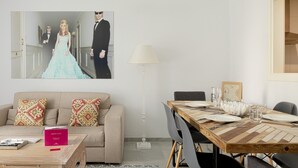A modern living room with a beige sofa, a wooden coffee table, and a dining table set for four. A framed photograph is on the wall, and a lamp is beside the table. - Pompidou 20 - 2 Rooms (Málaga)