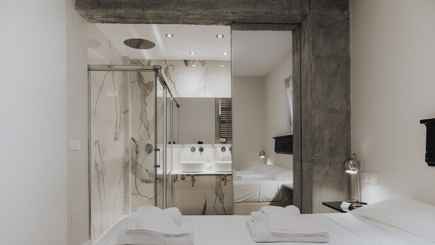 A modern bathroom with a glass shower enclosure, a large mirror, and a bed with towels. - Tribuna - Victoria 8 (Málaga)