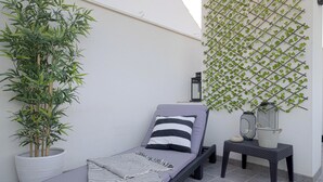 Eine Lounge-Ecke mit gepolstertem Sitz, einem Topf mit Pflanze, einer Wandpflanze und einem kleinen Tisch mit Laterne.