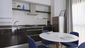 Eine moderne Küche mit einer zentralen Kochinsel, einem Essbereich mit blauen Stühlen und einem Kühlschrank.