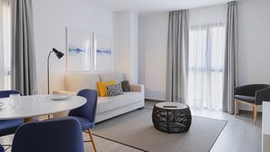Ein modernes Wohnzimmer mit einer Couch, einem runden Couchtisch, einem Esstisch mit Stühlen und einer Lampe.