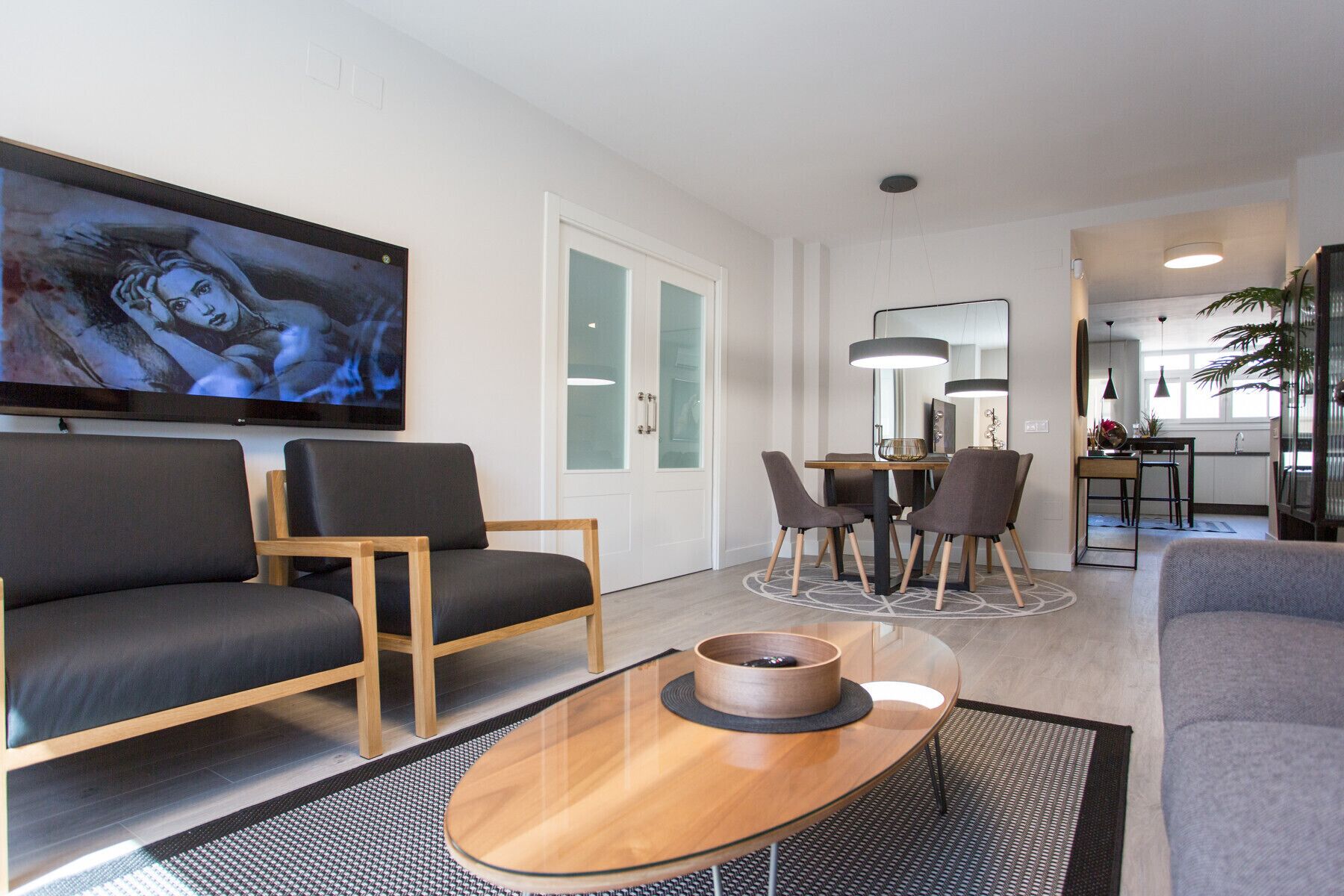 Una sala de estar moderna con un televisor de pantalla plana, un comedor con mesa y sillas, y una cocina al fondo.