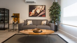 Una sala de estar moderna con un sofá gris, una mesa de centro de vidrio y una planta grande en maceta.