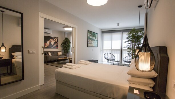 Un dormitorio moderno con una cama grande, un sofá, una mesa de comedor y un espejo.