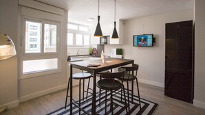 Una cocina moderna con una isla central, taburetes de bar, iluminación colgante y un televisor en la pared.