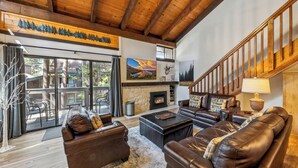 A spacious living room with leather sofas, a fireplace, and a wooden staircase.