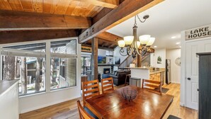 A spacious dining area with a wooden table and chairs, a chandelier, and a view of the outdoors through large windows.