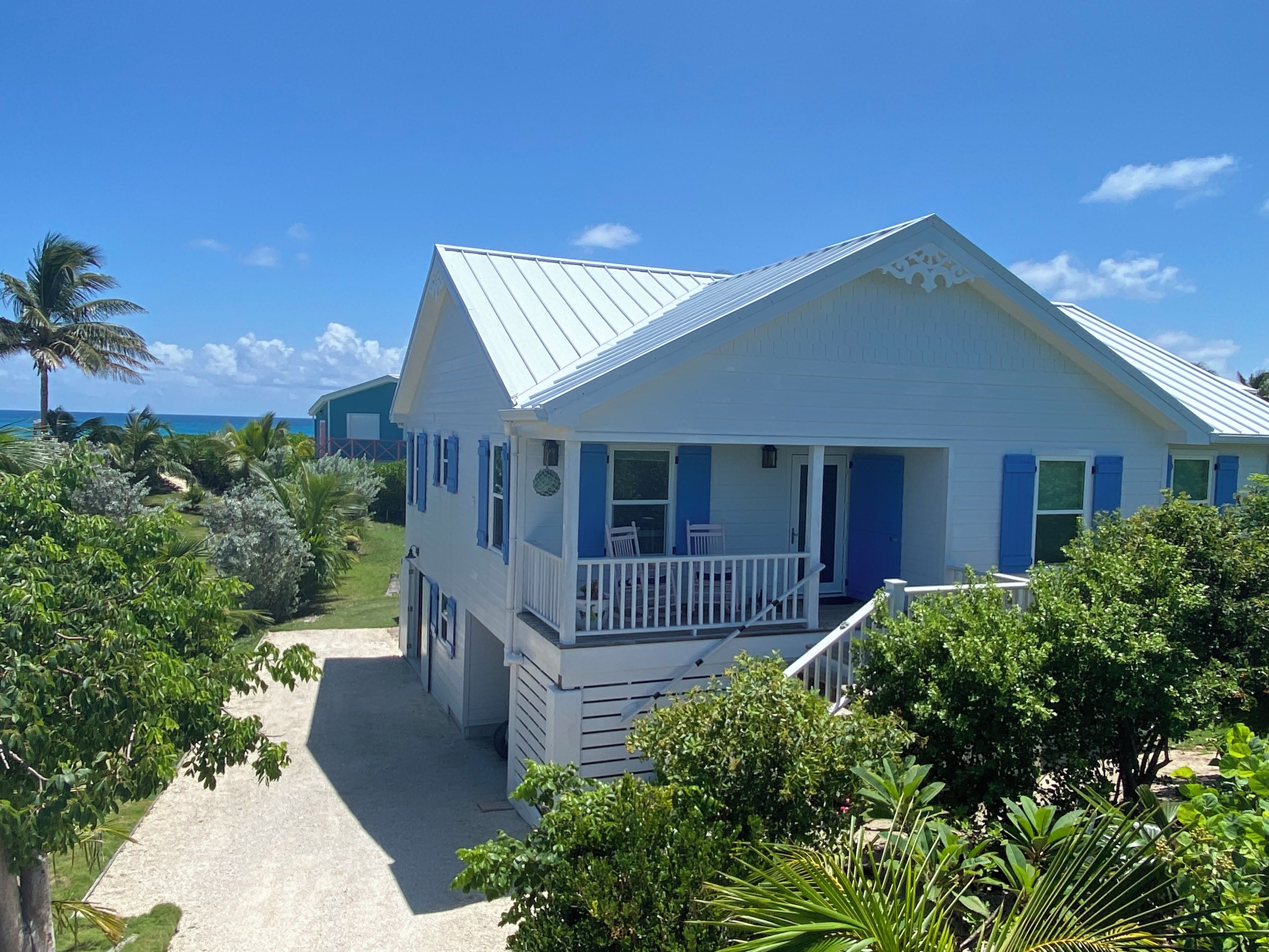 A white building with blue shutters, a balcony, and a view of the ocean.